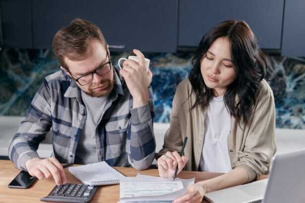 A couple reviewing household bills and budget using a calculator and laptop at their kitchen table.