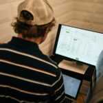 man in white and black striped polo shirt in front of monitor