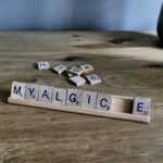 Scrabble tiles spell 'myalgic' on wooden surface