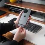 Person attaching accessory to iPhone on desk.