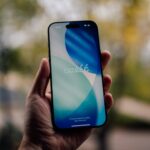 Hand holding a smartphone with a blue and white wallpaper.