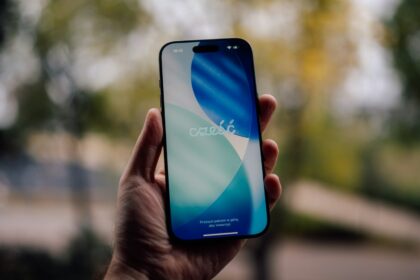 Hand holding a smartphone with a blue and white wallpaper.
