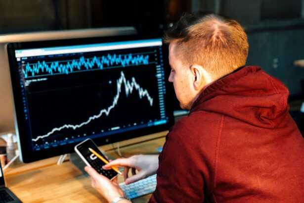 man holding black smartphone with flat screen monitor in front