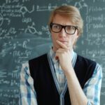 Man with glasses thinking in front of chalkboard